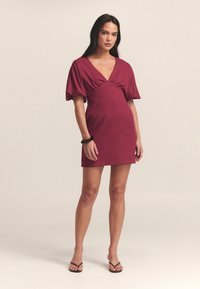 Vestido burdeos con corsé ajustado y mangas abullonadas, que presenta un escote en V y un dobladillo recto. Tela suave con texturas mínimas.