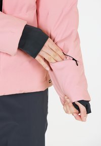 Rosa isolerad jacka med elastiska svarta muddar, med en ficka med dragkedja på ärmen och slät yta.