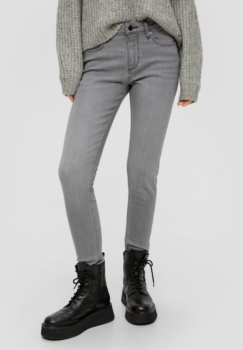 Jean skinny gris à texture lisse, avec cinq poches et une fermeture boutonnée, associé à des bottes de combat noires à lacets.