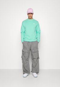 Sweatshirt verde menta, calças cargo cinzas com múltiplos bolsos, sapatilhas brancas e um boné rosa. Design simples com um corte relaxado.