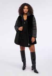 Prenda exterior negra que combina texturas acolchadas y de piel sintética, con cierre de cremallera, herrajes metálicos y diseño de longitud media.