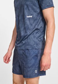 Marinblå sportoutfit bestående av en randig kortärmad skjorta och matchande shorts. Har "hummel"-logotyp och kontrasterande vita accenter.