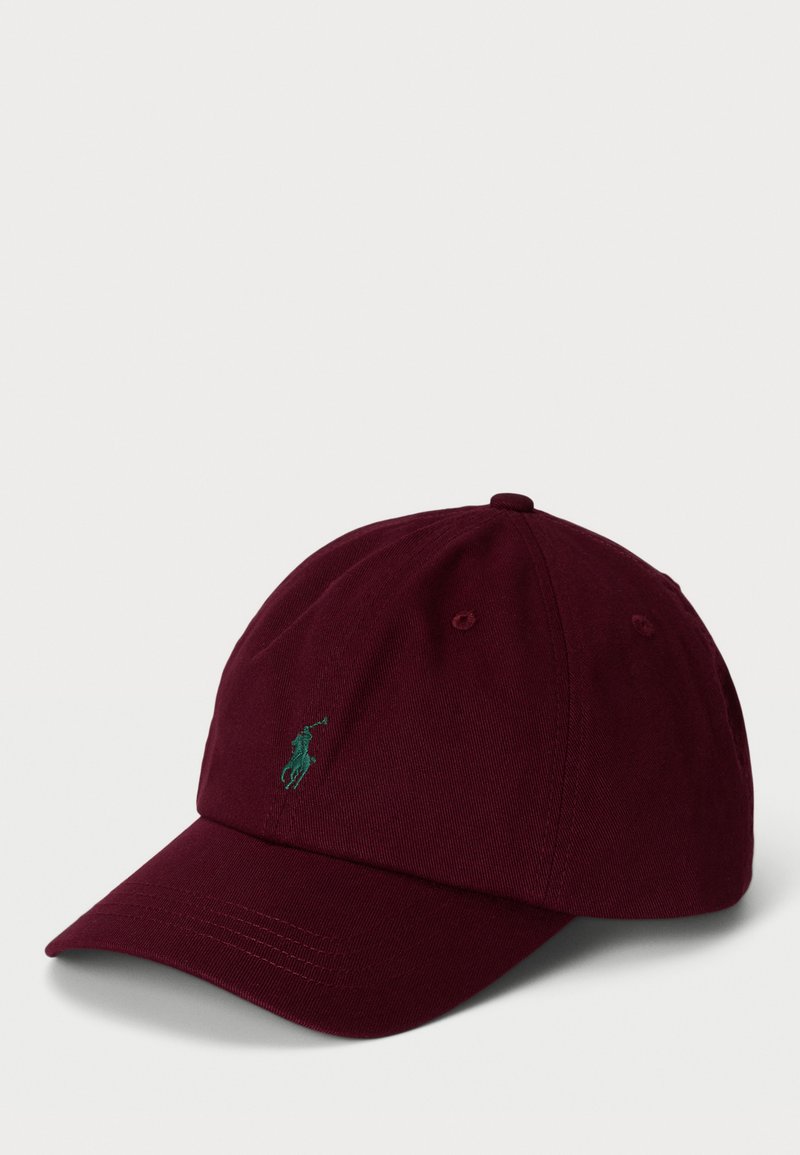 Burgunderfarget bomullsbasketcap med buet brem og grønn brodert logo foran. Har ventilasjonsøyne og justerbar stropp.