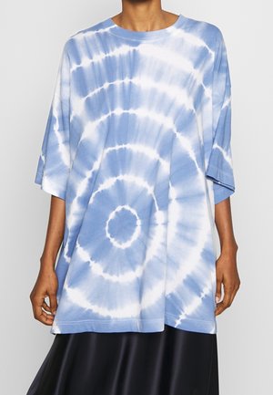 Osoba nosząca oversize niebiesko-biały t-shirt tie-dye z krótkim rękawem i wzorem koła oraz czarną spódnicę, widziana od szyi do bioder.