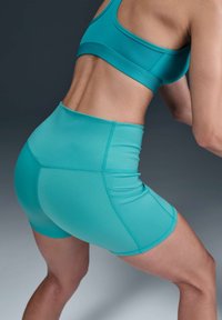Turkis atletisk sett som består av en tettsittende sports-BH og høy-livshorts, laget av elastisk stoff med jevn tekstur og sømdetaljer.