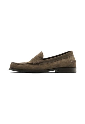 Mocassins en daim marron avec un bout arrondi et une bande sur le dessus. Présente une semelle plate en caoutchouc et des coutures discrètes.