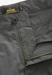 Grey fabric trousers with a button closure, zip fly, and a label reading "NEXT DURABLE GOODS 32R." Features a smooth texture and neat stitching.