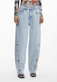 Hellblaue weite Jeans, mit einer geknöpften Seitennaht, die eine verblasste Denim-Textur und subtile Stickdetails aufweisen.