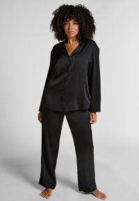 Zwart satijnen pyjama set bestaat uit een knoopsluiting met lange mouwen en een zak, en bijpassende wijde broek, beide met verticale strepen.