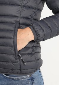 Chaqueta acolchada en gris oscuro, con diseño acolchado y puños elásticos, con un bolsillo lateral con cremallera para almacenamiento.