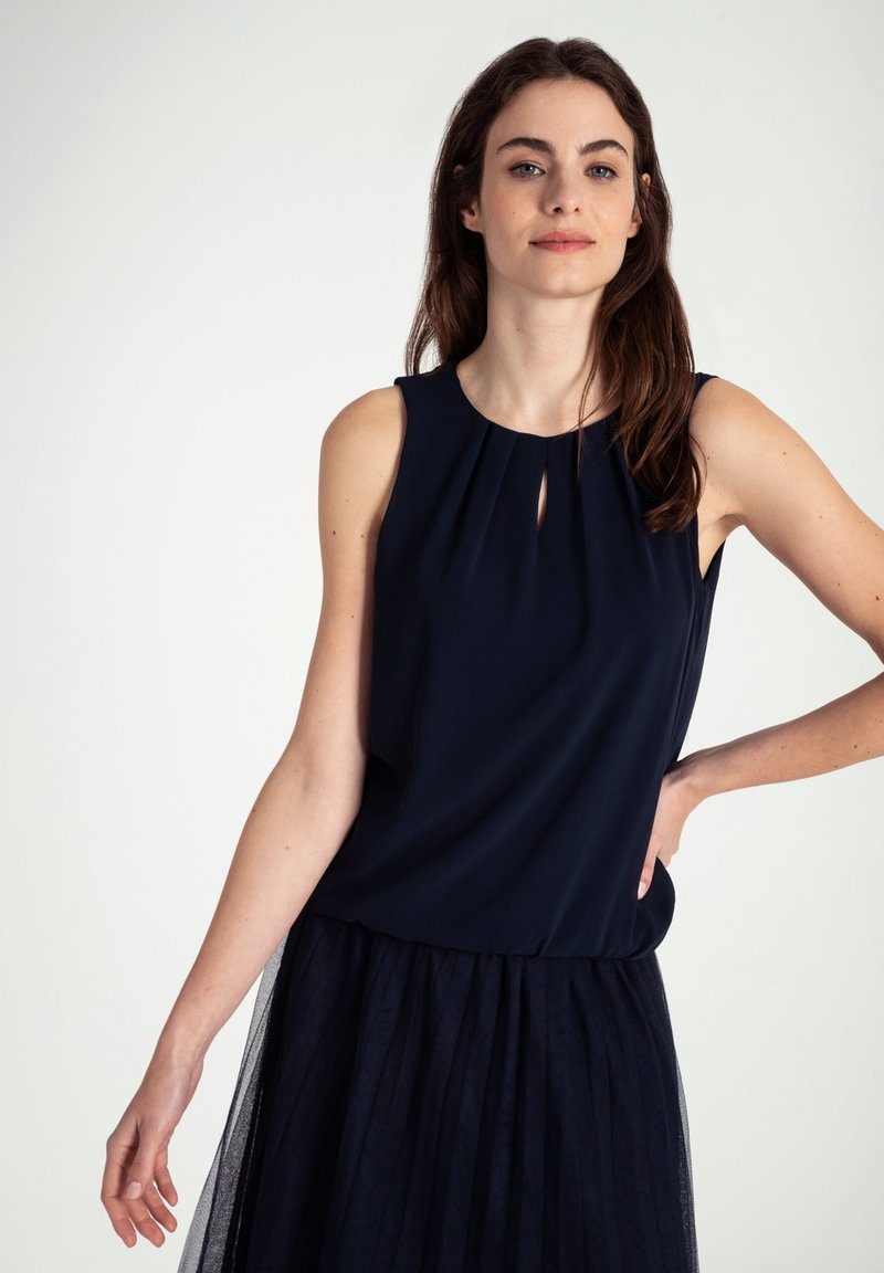 Marineblauw mouwloos topje met een sleutelsleufdetail bij de halslijn, gecombineerd met een bijpassende tule rok, met een gladde textuur.