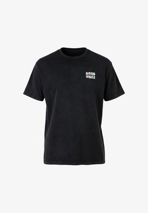 T-shirt noir à manches courtes avec petit texte pastel "GOOD VIBES" en lettres arrondies sur la partie supérieure gauche de la poitrine.