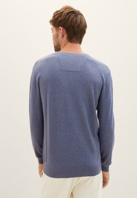 Blauwe trui gemaakt van zachte brei-stof. Heeft lange mouwen, een ronde halslijn en een horizontale naaddetail op de achterkant.