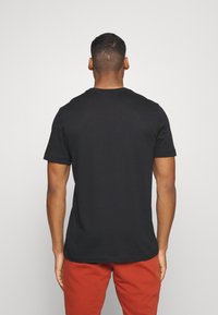 Camiseta negra de manga corta con cuello redondo, textura suave y ajuste relajado, combinada con pantalones rojos. Vista trasera visible.