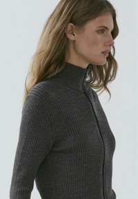 Dunkelgrauer, gerippter Pullover mit hohem Kragen und Reißverschlussdetail. Verfügt über lange Ärmel und eine figurnahe Silhouette, die den strukturierten Stoff betont.