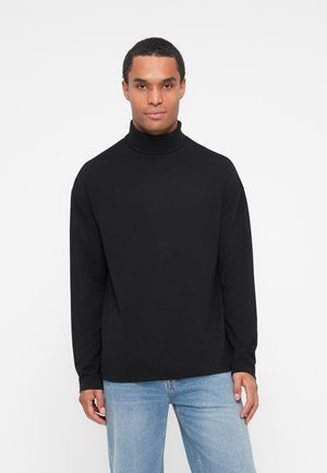 Zwarte coltrui van een gladde stof, met lange mouwen en een relaxte pasvorm. Gecombineerd met lichtblauwe jeans.