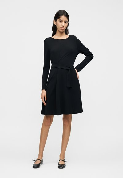 Μαύρο μακρυμάνικο φόρεμα από ομαλή υφή υφάσματος, με εφαρμοστό μπούστο, φαρδιά φούστα και αποσπώμενη ζώνη στη μέση. Διακοσμημένο με στρογγυλή λαιμόκοψη.