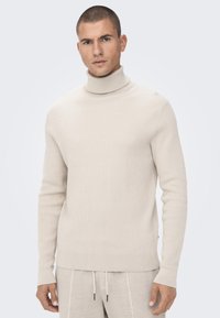 Beige, gerippter Rollkragenpullover mit langen Ärmeln und taillierter Passform, aus einem weichen Strickmaterial für Komfort und Wärme hergestellt.