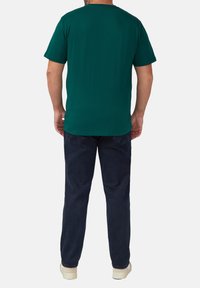 Donkergroene katoenen t-shirt met een ronde hals, korte mouwen en een rechte zoom, gedragen met donkerblauwe jeans en lichtgekleurde schoenen.