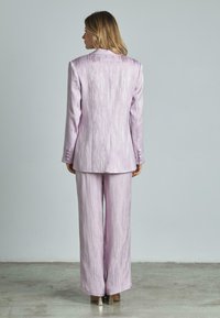 Helles lila Anzug mit strukturierter, glänzender Oberfläche. Die Jacke hat ein Revers mit Notch und drei Knöpfe an jedem Ärmel; die Hose hat einen weiten Beinansatz.
