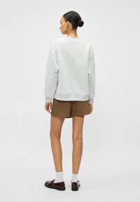 Gaiši pelēks džemperis ar noslīpētām pleciem, aprocēm uz piedurknēm un apaļu apakšmalu. Kombinēts ar brūniem rūtainiem šortiem un melu apavu pāri.