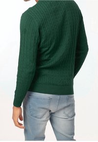 Pull vert en maille torsadée avec poignets et ourlet côtelés, porté sur un jean bleu clair, montrant le tissu texturé et une coupe ajustée vue de dos.