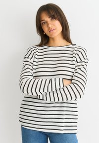 Striped sweater in cream and black with long sleeves, round neckline, and textured knit pattern, paired with blue jeans.