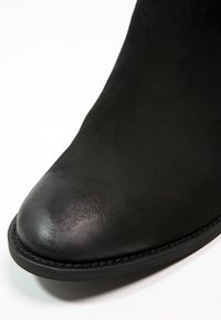 Bottines en cuir noir avec un bout arrondi, texture lisse et semelle en caoutchouc cousue. L'accent est mis sur le matériau supérieur.