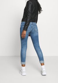 Tunna blå denimjeans med lätt slitage och uppvikta benslut, kombinerade med en svart läderjacka och vita sneakers.