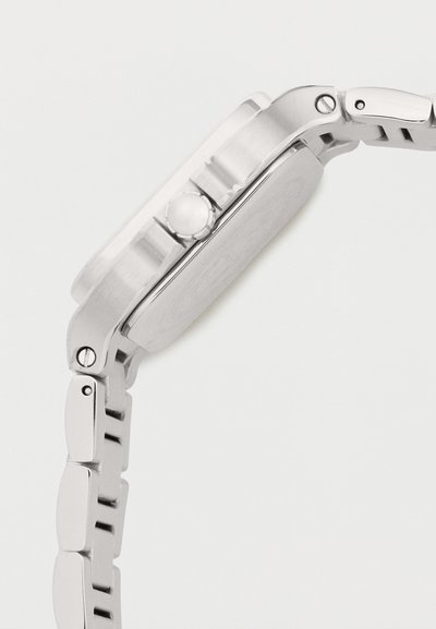 Bracelet de montre en métal argenté et vue latérale du boîtier avec bouton couronne sur un fond clair uni.