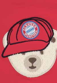 Red textile featuring an embroidered polar bear face with a textured, cream-colored muzzle and a red cap displaying FC Bayern München logo.