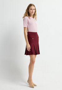 Rosa kortärmad topp kombinerad med en bordeauxfärgad plisserad kjol med två framfickor och knappar i guldton. Beiga lägenheter fullbordar outfiten.