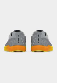 Ζευγάρι γκρι πλεκτά αθλητικά παπούτσια με πορτοκαλί και κίτρινες σόλες, εμφανιζόμενα από πίσω, με το όνομα της μάρκας "Altra" στις φτέρνες.