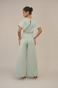 Macacão verde claro com pernas largas, mangas tipo capa e fecho de botão nas costas. Tecido suave e design minimalista com um brilho subtil.