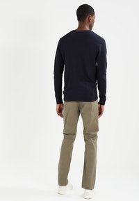 Suéter de manga larga azul marino con cuello redondo, combinado con pantalones chinos de color verde oliva claro. El modelo está de espaldas, mostrando un diseño sencillo.