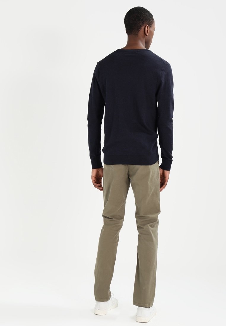 Suéter de manga larga azul marino con cuello redondo, combinado con pantalones chinos de color verde oliva claro. El modelo está de espaldas, mostrando un diseño sencillo.