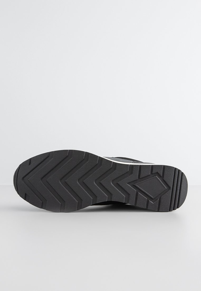 Zwarte sneakersole met een zigzag loopvlakpatroon, gemaakt van rubber. Heeft een plat ontwerp en is textuur voor grip, benadrukt door een witte streep.