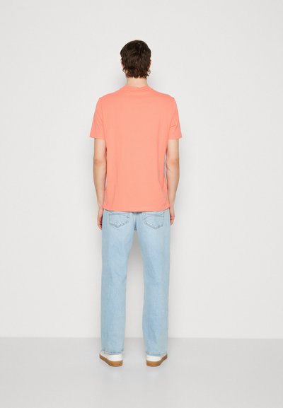 T-shirt corail à manches courtes, en coton, coupe décontractée, associé à un jean en denim bleu clair, jambe droite, poches arrière, baskets blanches.