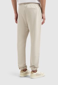 Lichtbeige sweatpants met een elastische tailleband, taps toelopende manchetten en een achterzak. De stof lijkt zacht en heeft een gladde textuur.