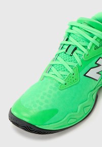 Lysegrøn New Balance sneakers med mesh-overdel, sort sål og snørebånd bundet, vist fra frontvinkel på hvid baggrund.