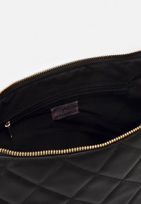 Musta tikattu laukun sisusta, jossa on kullanvärinen vetoketju. Sisältää pienen mustan vetoketjullisen taskun ja etiketin, jossa lukee "ANNA FIELD".