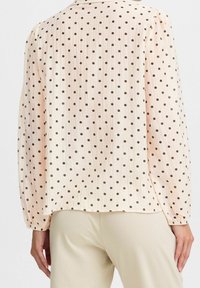 Blusa rosa chiaro con pois neri, texture plissettata, maniche lunghe e vestibilità comoda, caratterizzata da un orlo arrotondato e spalle a palloncino.