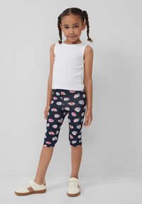 Witte mouwloze top, marineblauwe leggings met kleurrijk schelpatroon en witte sneakers met tan accenten, met een comfortabele pasvorm.