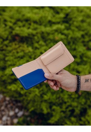 Beige and blue bi-fold wallet with card slots and a snap closure. Smooth texture, contrasting color, and embossed branding detail.