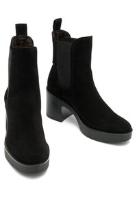 Botines de ante negro con un tacón ancho, paneles laterales elásticos y una puntera redonda. La suela es lisa y ligeramente texturizada.