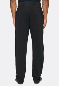 Juodos sportinės kelnės su elastinga juosta, tiesiomis kojomis ir minkšta, lygi tekstūra. Nėra matomų raštų ar metalinių detalių.