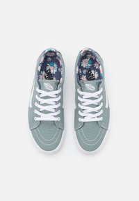 Green canvas sneakers with white laces and stitching. The interior features a colorful floral pattern. Rubber sole, casual design.