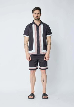 Ensemble de chemise à manches courtes boutonnée et de shorts en tissu foncé avec des rayures verticales blanches et roses. Des sandales noires à enfiler complètent le look.