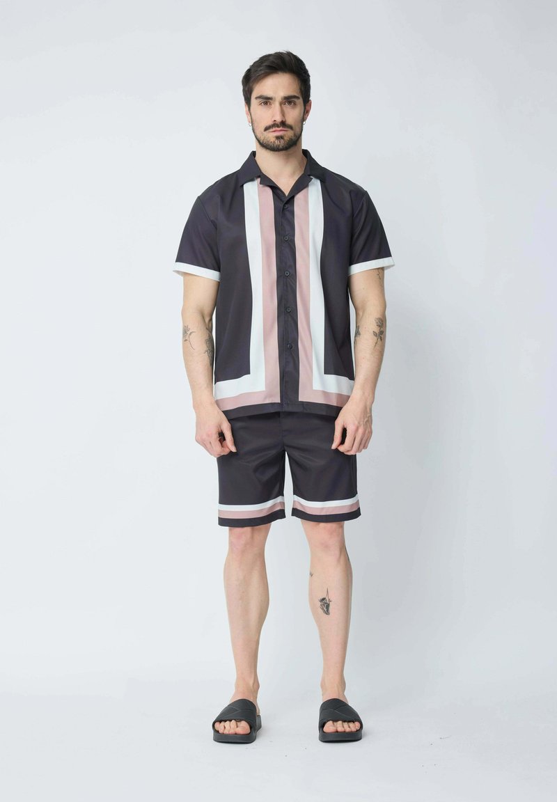 Ensemble de chemise à manches courtes boutonnée et de shorts en tissu foncé avec des rayures verticales blanches et roses. Des sandales noires à enfiler complètent le look.