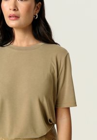 Beigu īsām piedurknēm T-krekls, kas izgatavots no gludas auduma, ar apaļu apkakli un brīvu piegriezumu. Minimalistisks dizains ar vienkāršu faktūru.